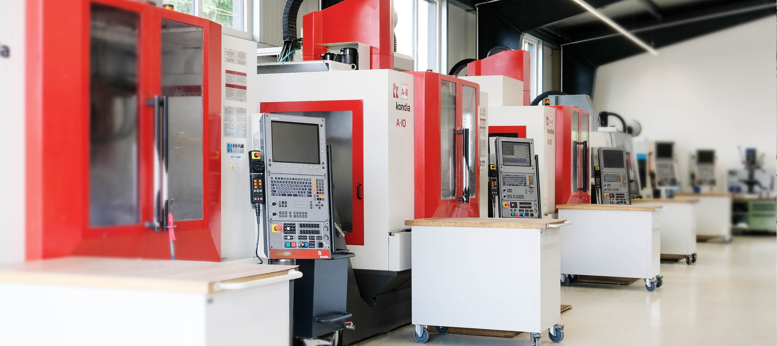 Reihe von CNC-Fräsmaschinen mit Steuerpulten in einer Werkstatt, links Text 'CNC ZERSPANUNG' und 'WU Mechanische Werkstätte'.