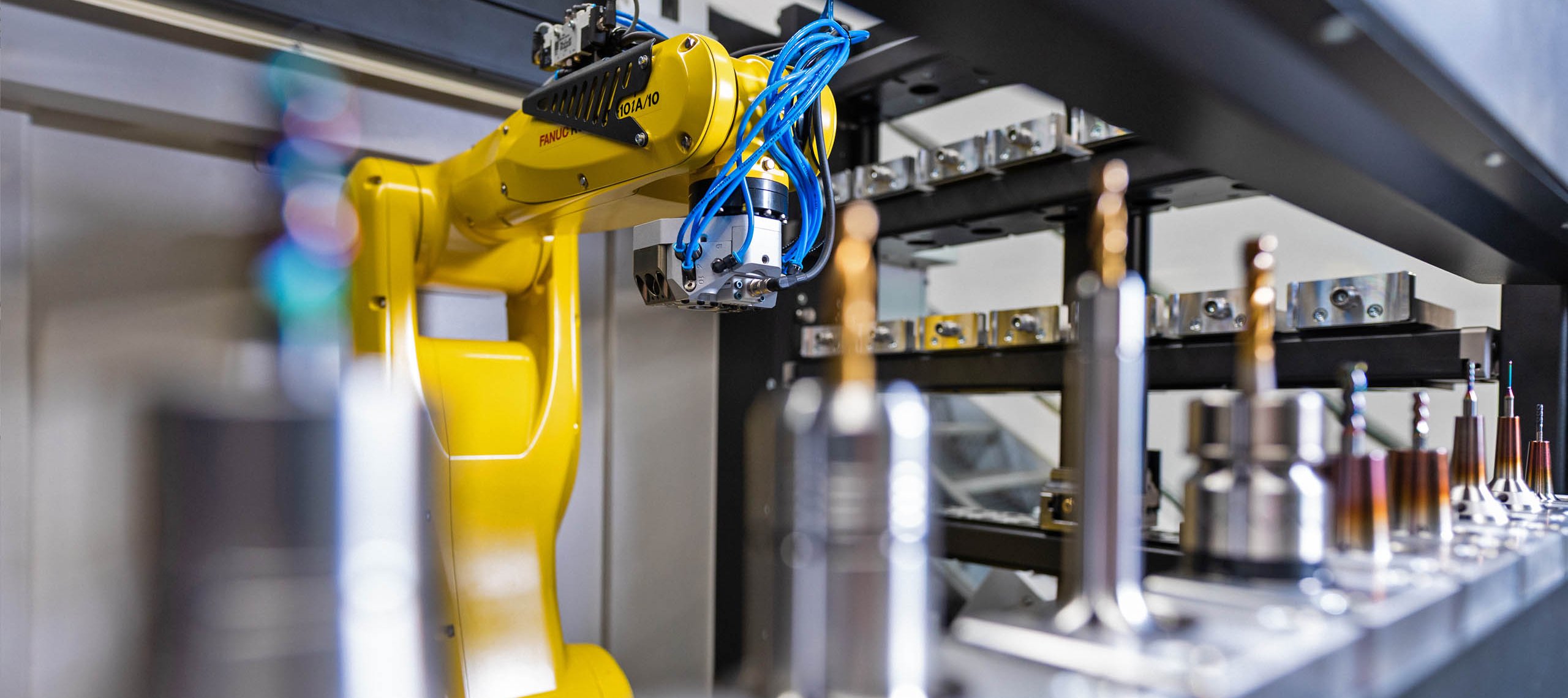 Gelber Industrieroboterarm in Fertigungsanlage mit Metallteilen auf Förderband, Text 'AUTOMATION & ROBOTIK Die RZ-Reihe entlastet Ihre qualifizierten Mitarbeiter'